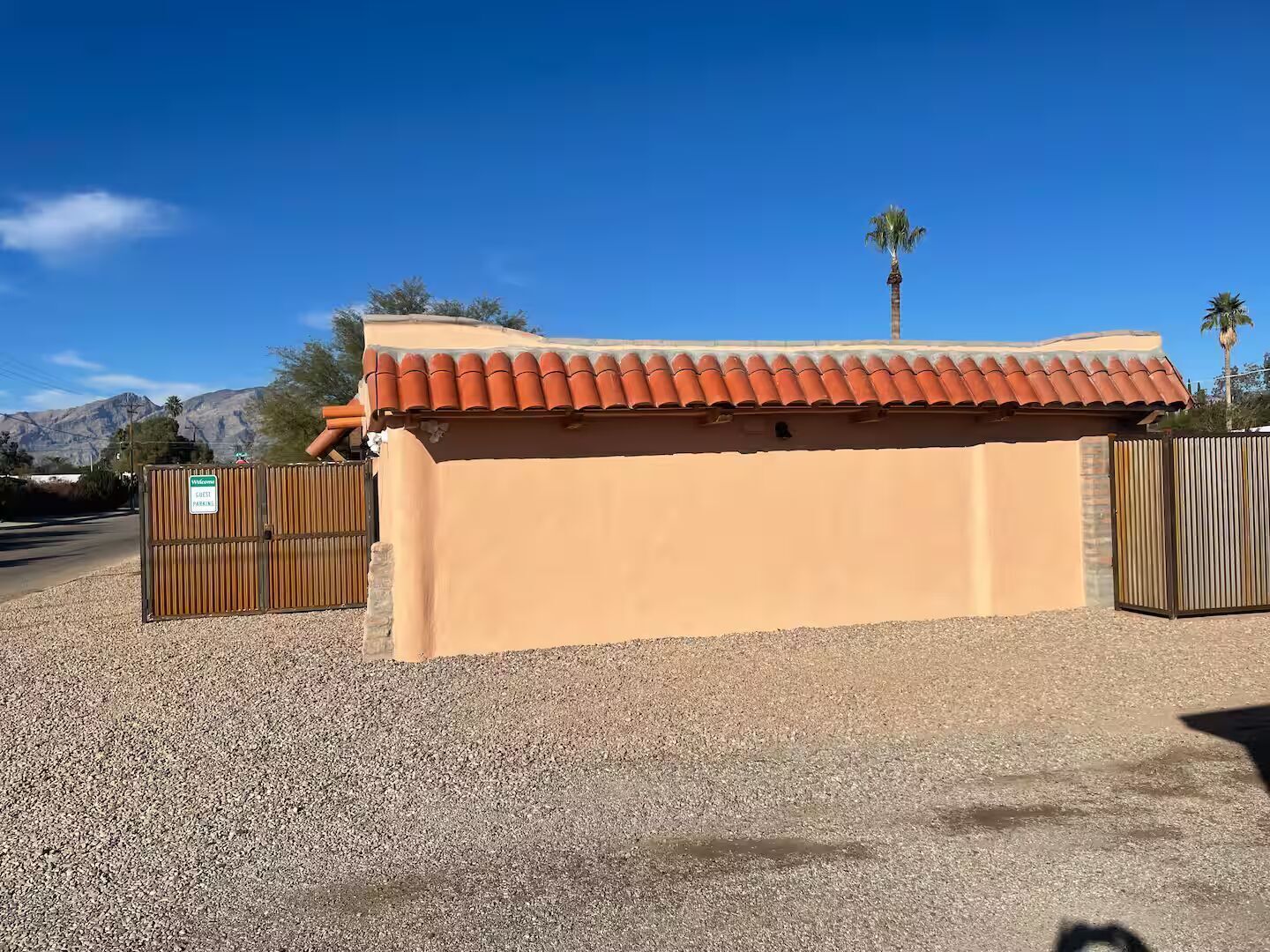 A building with a red-tiled roof and beige walls, a gravel driveway, and a gated entrance.