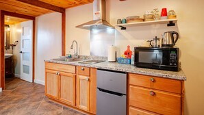 Una cocina con armarios de madera, una campana extractora de acero inoxidable, un microondas y una estantería con vajilla y una tetera.