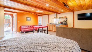 Una habitación acogedora con una cama, un sofá rojo, una mesa de comedor y una kitchenette.