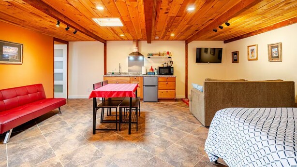 Una habitación acogedora con un sofá rojo, una mesa de comedor con sillas, una kitchenette, una cama y un televisor en la pared.