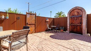 Un patio al aire libre con piso de ladrillo, una mesa de madera, sillas de mimbre y una puerta grande de madera.