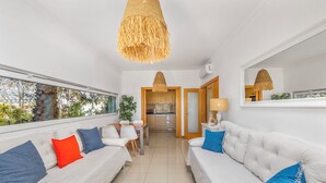 Un salon moderne avec des canapés blancs, un coin repas et une cuisine visible à travers une porte ouverte.