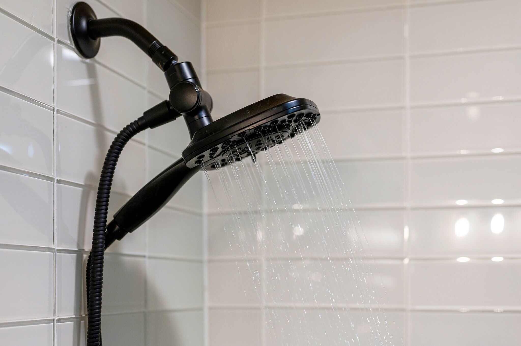 Un soffione con acqua che scorre, fissato a una parete piastrellata.