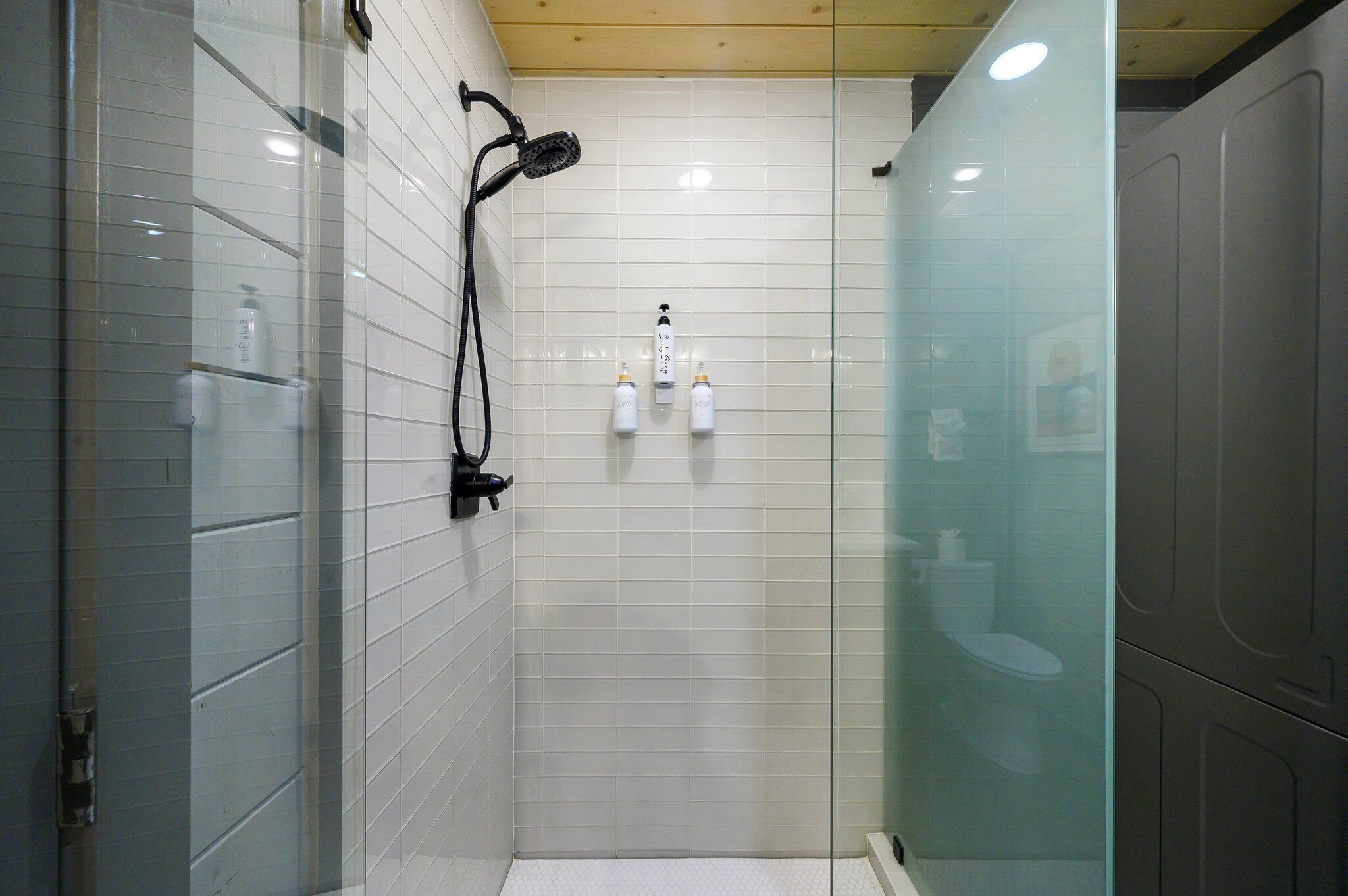 Ein modernes Badezimmer mit weißen Fliesen, einer Duschkabine aus Glas und einer Toilette.