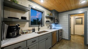A modern kitchen with a large window, stainless steel appliances, and grey cabinetry.