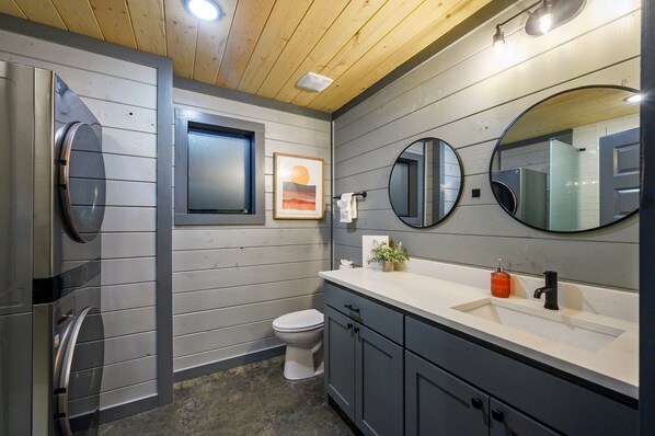 A modern bathroom with a wooden ceiling, a toilet, a sink with a mirror, and a wall-mounted towel rack.
