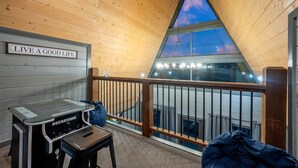 A cozy room with a wooden ceiling, a sign saying "LIVE A GOOD LIFE", a piano, and a view of the sky through a triangular window.