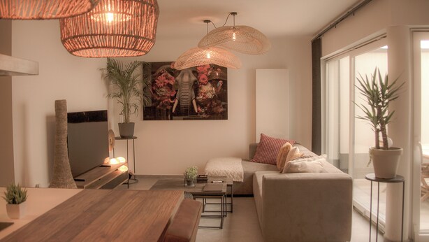 A modern living room with a sofa, a coffee table, and a TV. There are wicker lampshades and a potted plant.