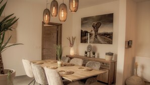 A dining area with a wooden table, cushioned chairs, and pendant lighting.