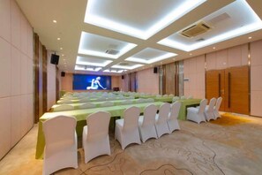 A conference room with a long table, white chairs, and a stage with a blue backdrop. - Fei Li International Hotel (Guangzhou)