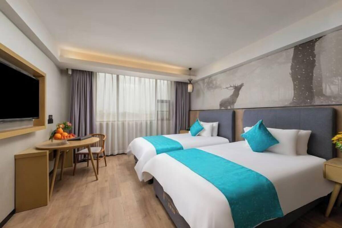 A hotel room with two beds, a desk, a chair, a TV, and a large window with curtains.