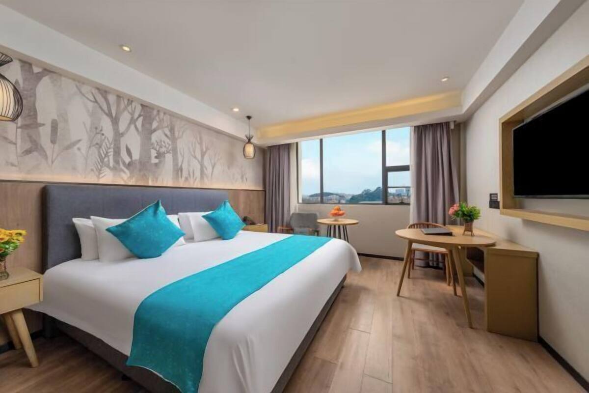 A hotel room with a large bed, a small table, a chair, a TV, and a window with a view.