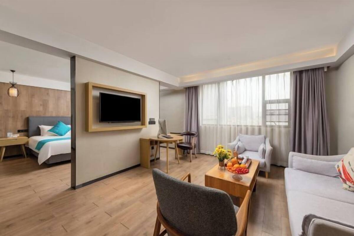 A modern hotel room with a bed, a TV, a dining area with a table and chairs, and a sofa.