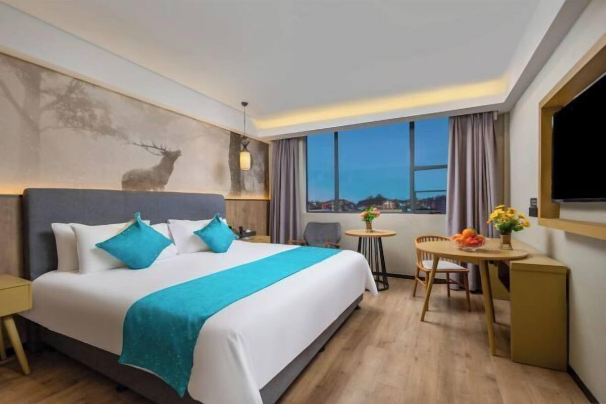 A modern hotel room with a large bed, a small table with flowers, a chair, and a TV.