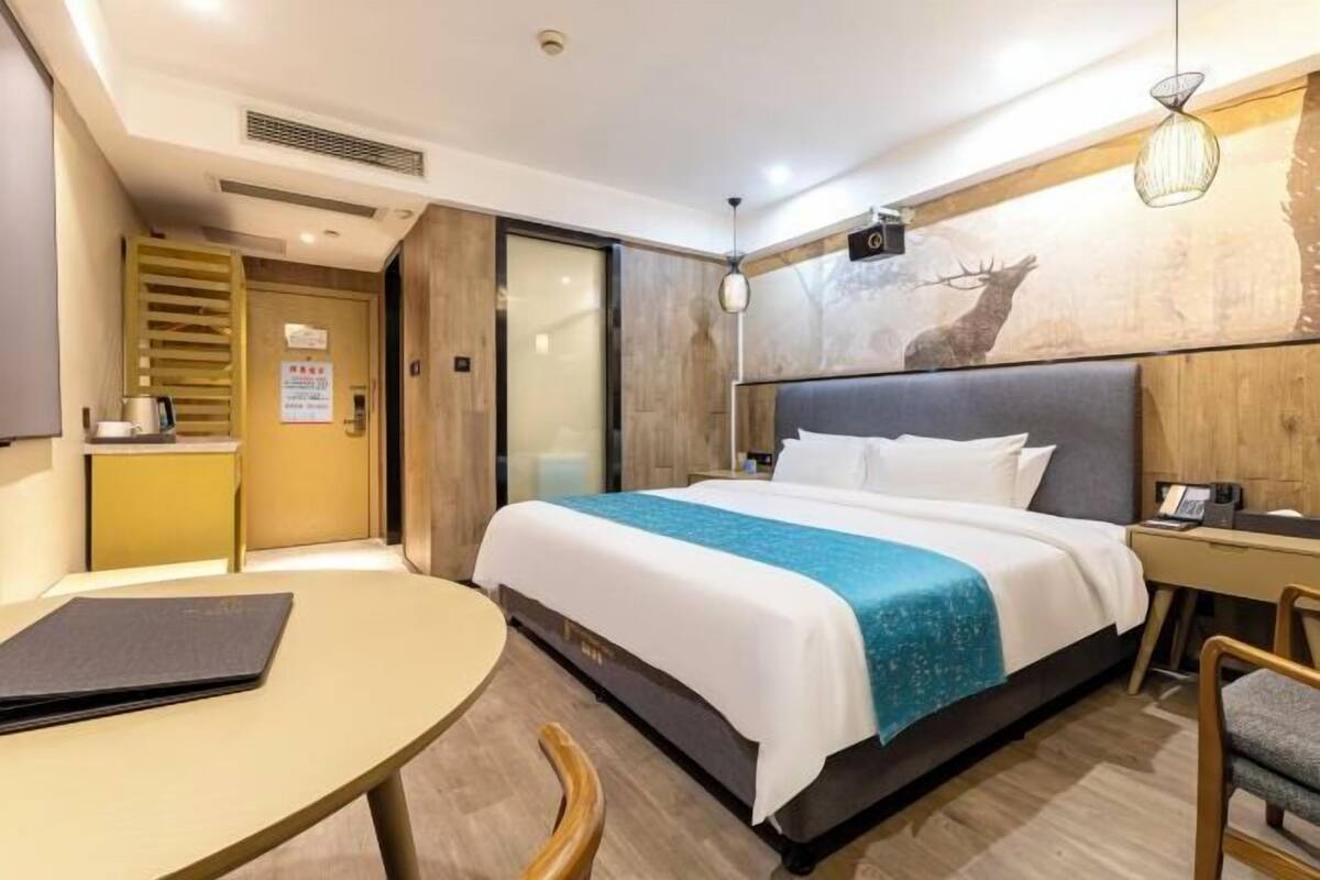 A hotel room with a bed, desk, chair, and a wall with a deer painting.