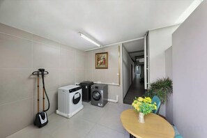 A compact room with a washing machine, a vacuum cleaner, and a small table with a vase of flowers. - Fei Li International Hotel (Guangzhou)