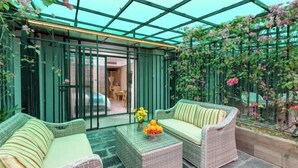 Una veranda con mobili in vimini, un tavolino in vetro e vista su un giardino con piante rampicanti.