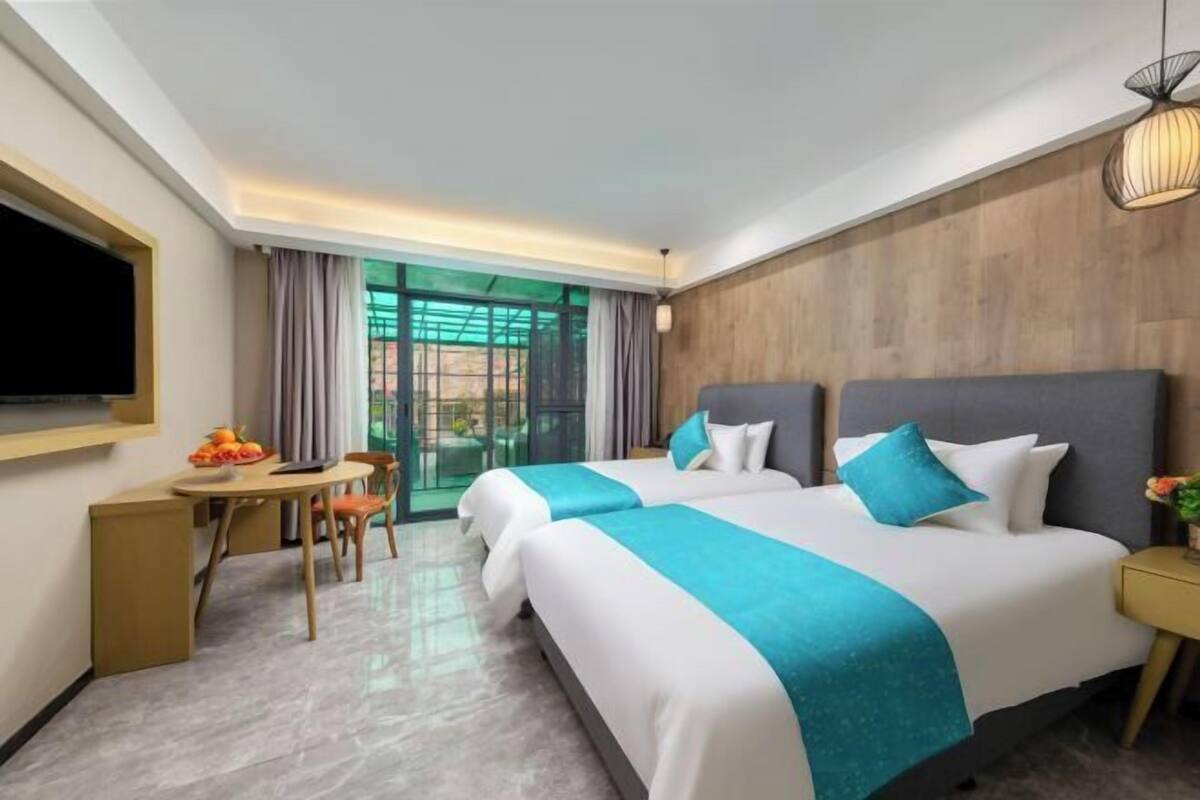 A hotel room with two beds, a desk, a chair, and a TV.