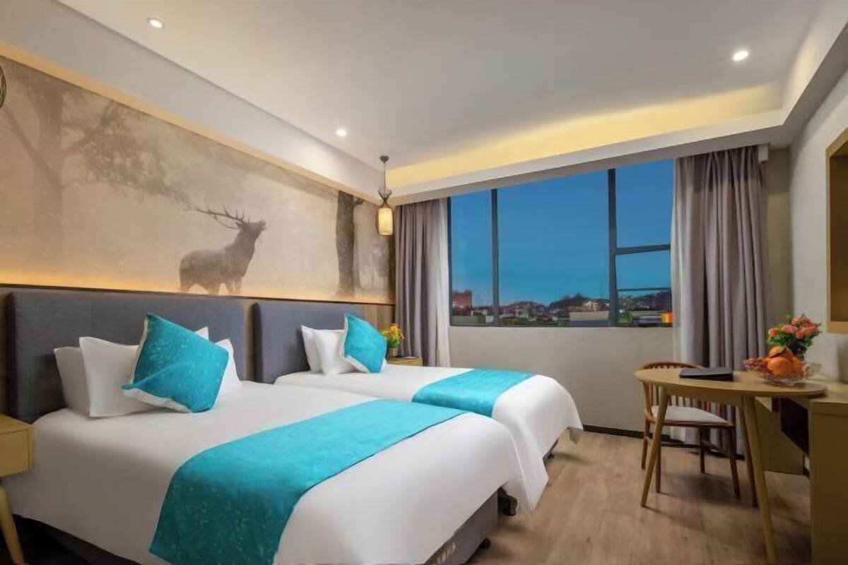A hotel room with two beds, a desk, and a view of the cityscape.