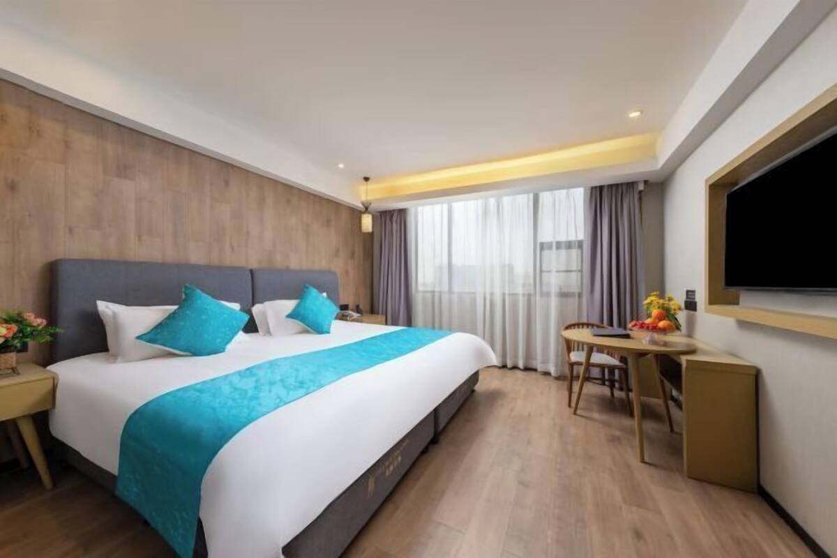 A hotel room with a bed, a desk, a chair, a TV, and a window with curtains.