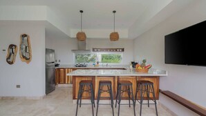 A modern kitchen with a large island, bar stools, a flat-screen TV, and a window with a view of greenery. - Incredible private property: 2 apartments with wifi, pool and nearby cenote (Tulum)