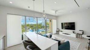 Ein modernes Wohnzimmer mit großem Fernseher, einer Essecke mit Blick auf einen Pool und einem Balkon mit großen Fenstern.