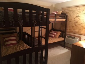 A bunk bed room with two beds, a heater, and a window with blinds. - Golf course condo, 10 min to Torch Lake, w/pool, hot tub and sauna! (Mancelona)