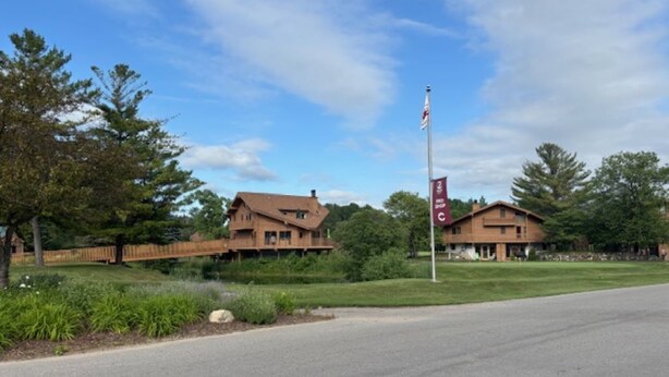 A two-story building with a flagpole in front. - Golf course condo, 10 min to Torch Lake, w/pool, hot tub and sauna! (Mancelona)