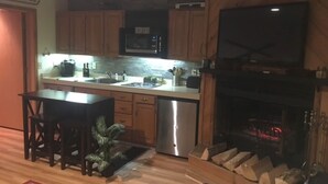 A kitchen with wooden cabinets, a microwave, a sink, a dishwasher, and a television mounted above the fireplace. - Golf course condo, 10 min to Torch Lake, w/pool, hot tub and sauna! (Mancelona)