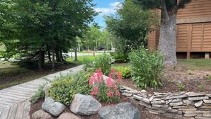 A landscaped garden with a wooden pathway, large rocks, and flowering plants. - Golf course condo, 10 min to Torch Lake, w/pool, hot tub and sauna! (Mancelona)