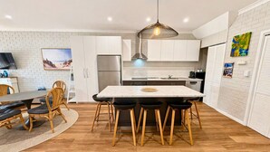 A modern kitchen with white cabinets, a central island with stools, a hanging light fixture, and a dining area with a table and chairs.