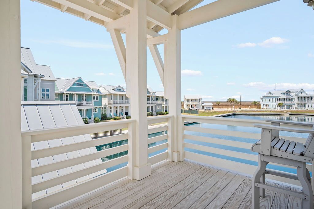 Una terraza de madera con piscina, barandillas blancas y casas al fondo.