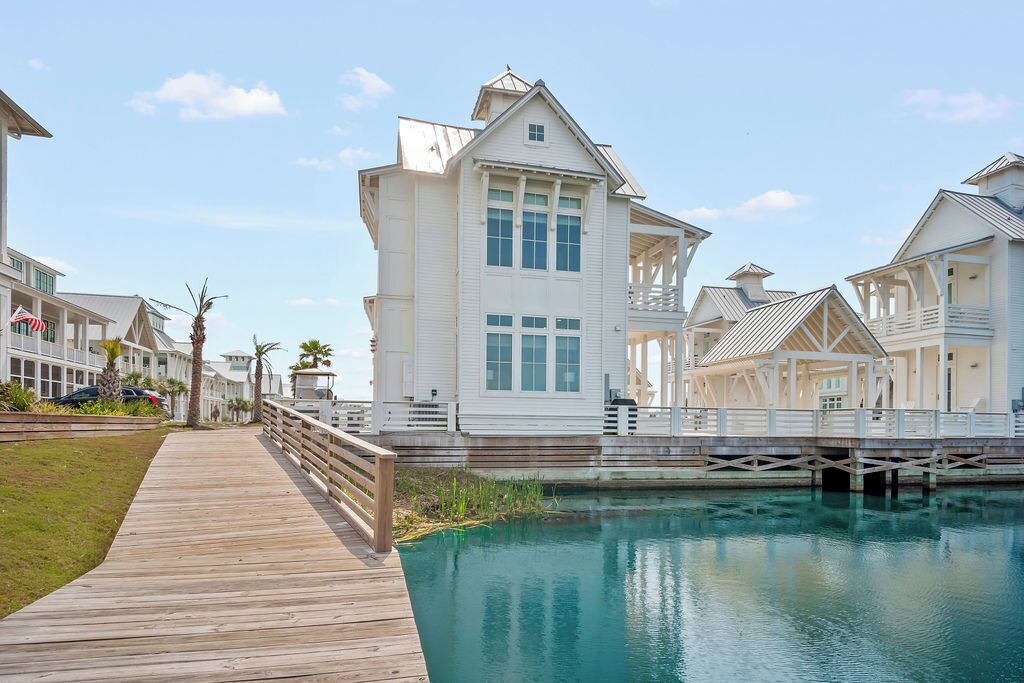 A waterfront property with a wooden boardwalk leading to a white building with multiple windows and balconies.