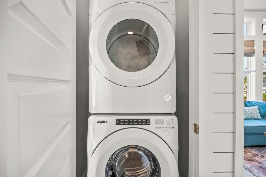 A stacked washer and dryer unit in a laundry room with a white door and a view of a blue couch in the background.