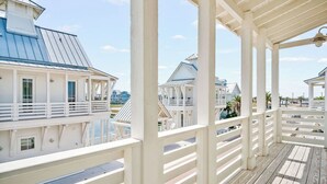 Eine überdachte Holzterrasse mit weißen Geländern, mit Blick auf eine Marina mit Booten und Gebäuden.