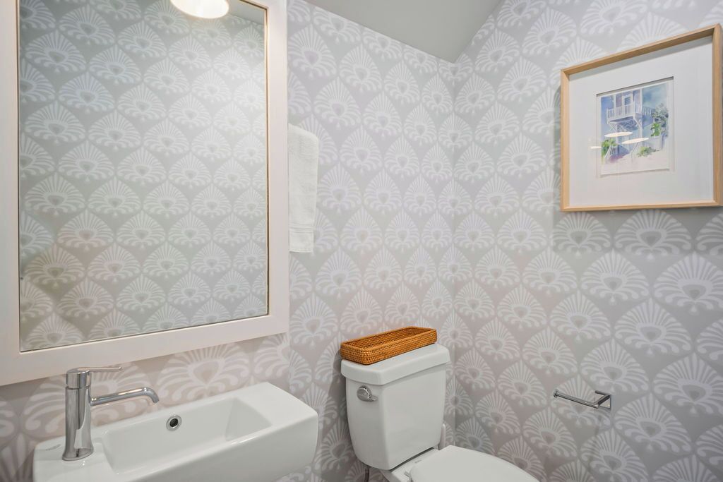 A bathroom with a patterned wallpaper, a white sink, and a framed picture on the wall.