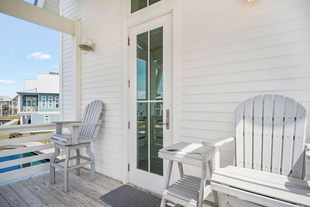 A covered porch with two Adirondack chairs and a small table, overlooking a pool.