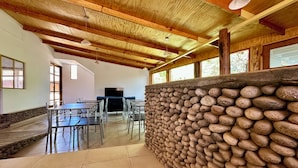 A spacious room with a stone wall, wooden ceiling beams, and a large flat-screen TV. - hostal qachisolcor (San Pedro de Atacama)