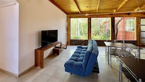 A living room with a TV, sofa, dining table, and large windows. - hostal qachisolcor (San Pedro de Atacama)