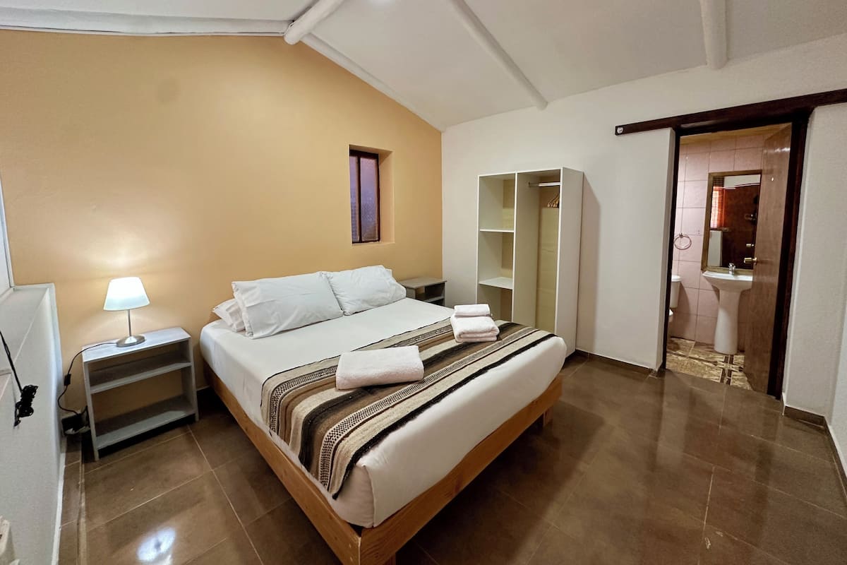 Un dormitorio con cama, mesita de noche, lámpara, armario y vistas al baño.