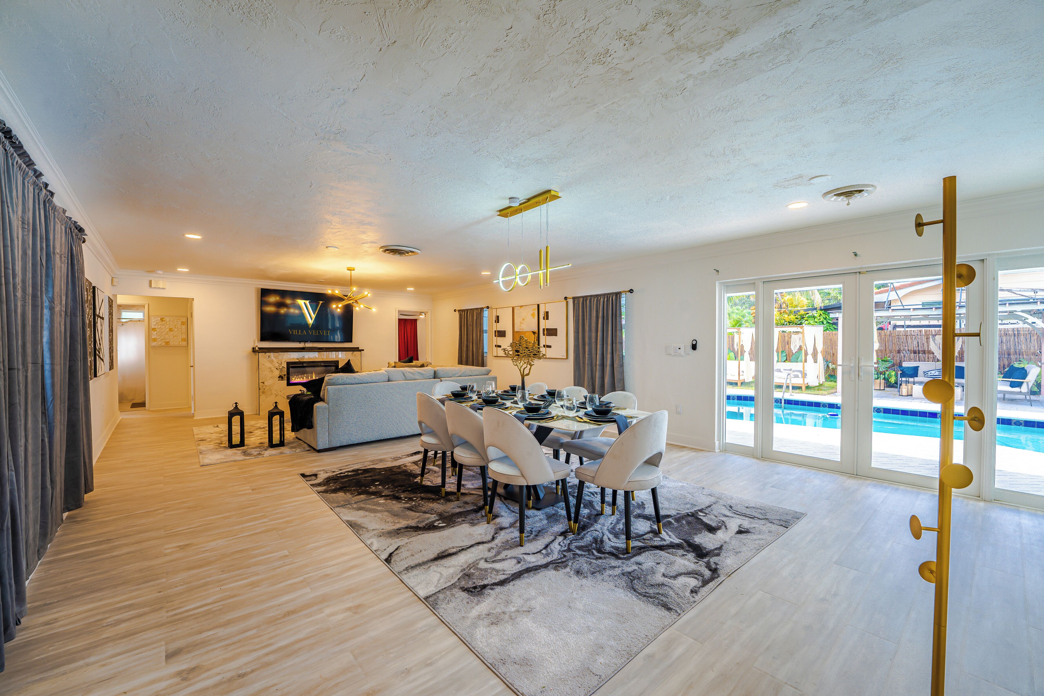 A modern living room with a dining area, a fireplace, and a pool view.