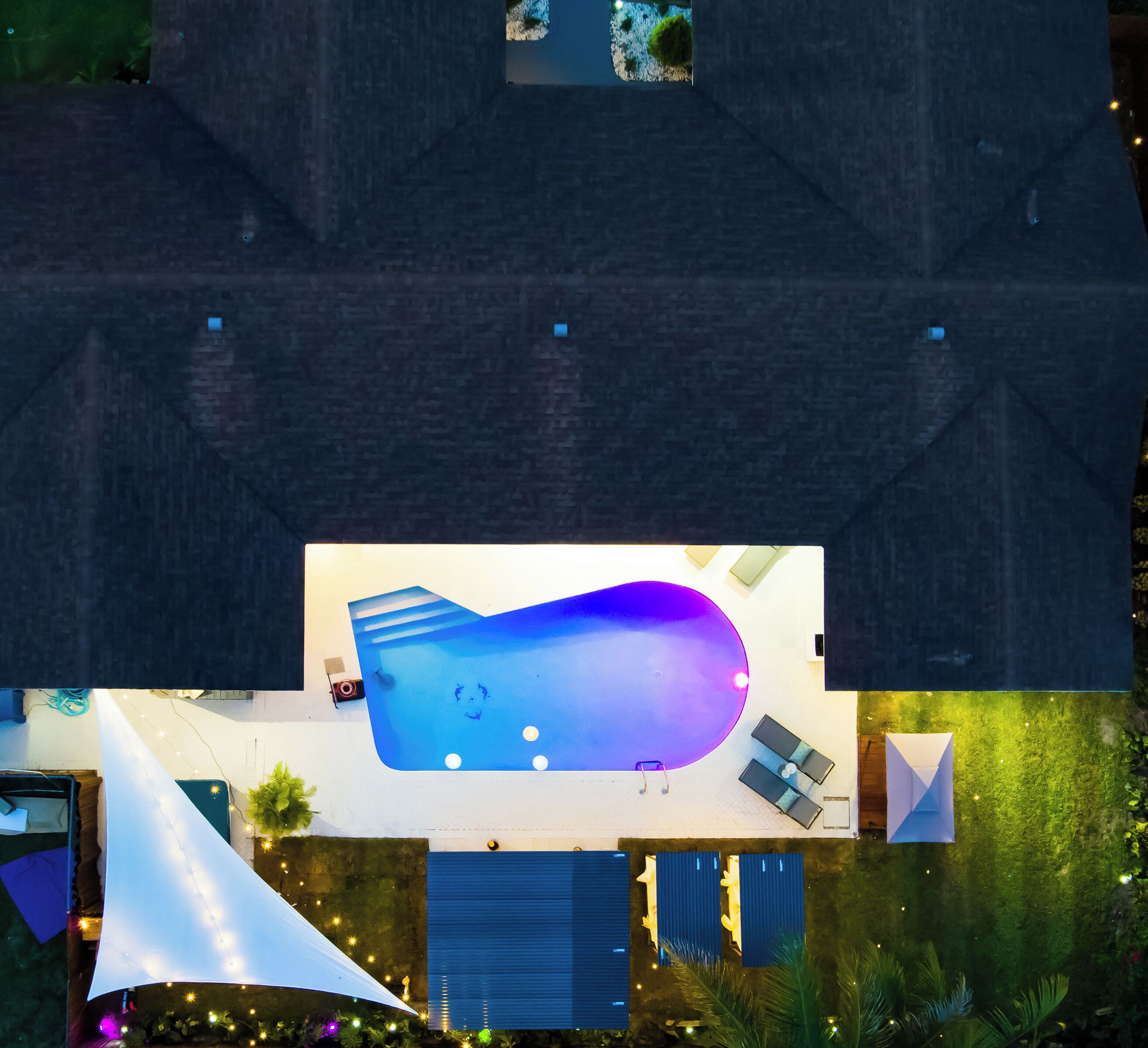 An aerial view of a modern house with a large swimming pool, a covered patio, and a well-maintained garden.