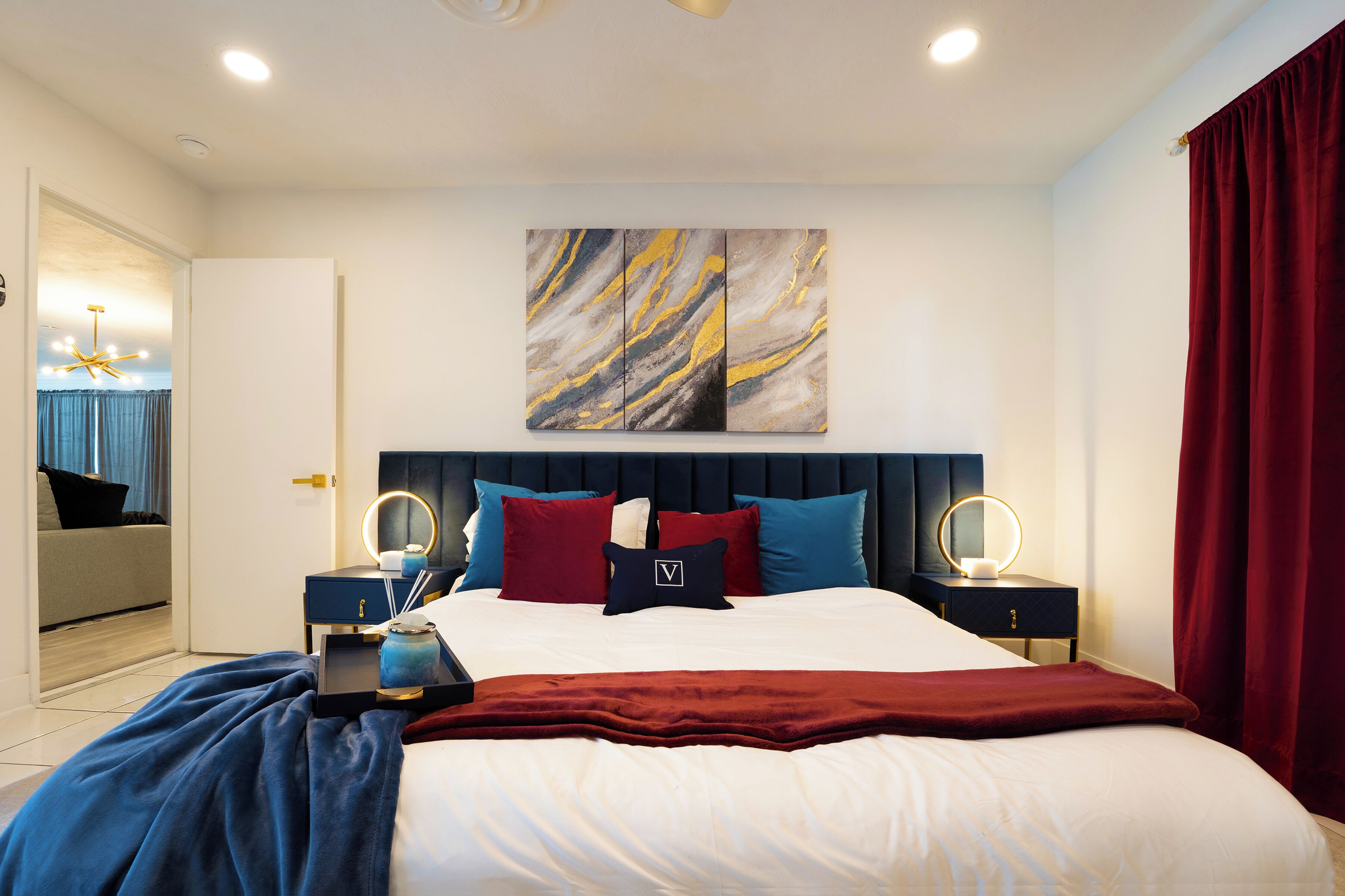 A modern bedroom with a large bed, two bedside tables with lamps, a headboard, and a wall-mounted artwork.