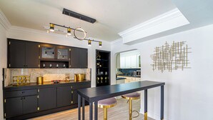 Een moderne keuken met donkere kastjes, een marmeren aanrechtblad en gouden accenten. Er is een bargedeelte met krukken en een hanglamp.