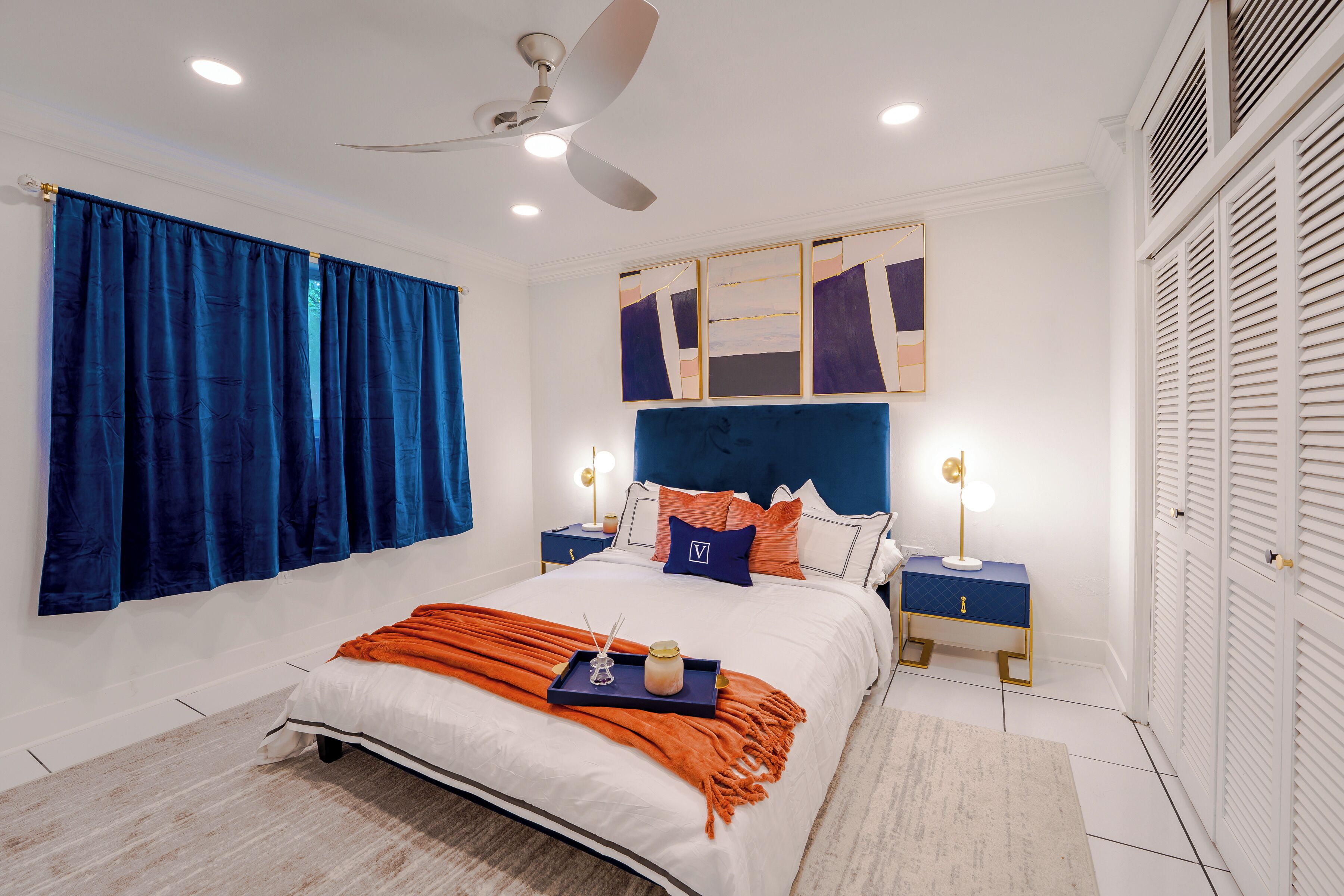 Un dormitorio moderno con una cama grande, un ventilador de techo y una mesita de noche con lámpara.