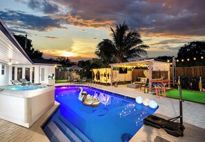 Una piscina con hidromasaje y sillones de descanso, rodeada por una terraza con aro de baloncesto y un área de estar cubierta.