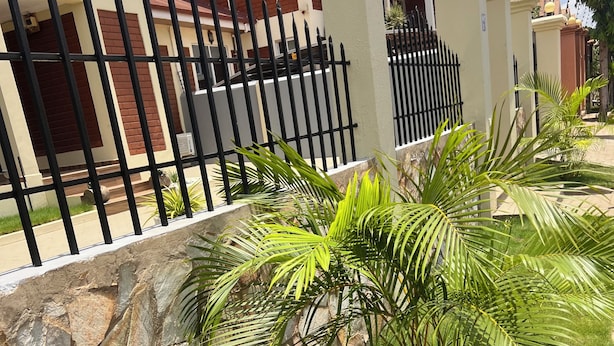 Un barrio residencial con un muro de piedra, cerca metálica negra y exuberantes palmeras verdes.