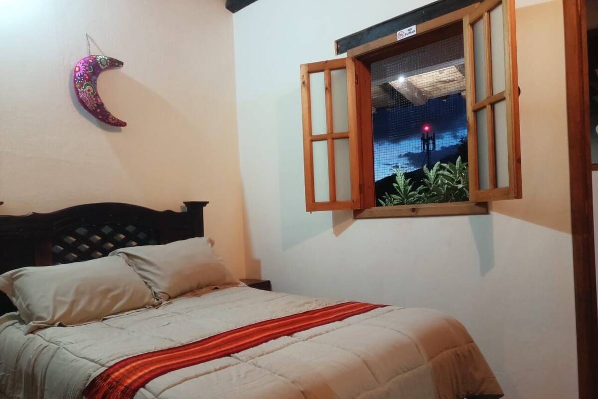 Um quarto com cama, janela com vista para a paisagem noturna e uma lua crescente decorativa na parede.