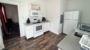 A compact kitchen with white cabinetry, a microwave, a stove, a refrigerator, and a coffee maker.