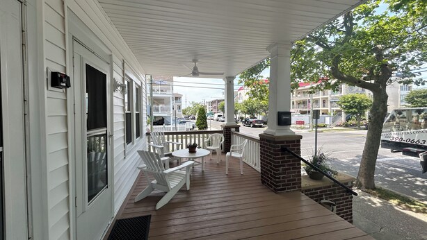 A covered porch with white chairs and a small table, a brick fireplace, and a view of the street.